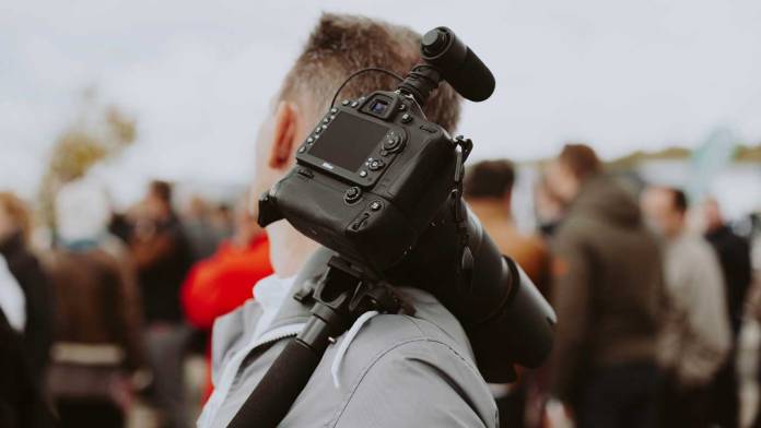 On-the-go-Enews Videographer in crowd with camera on tripod
