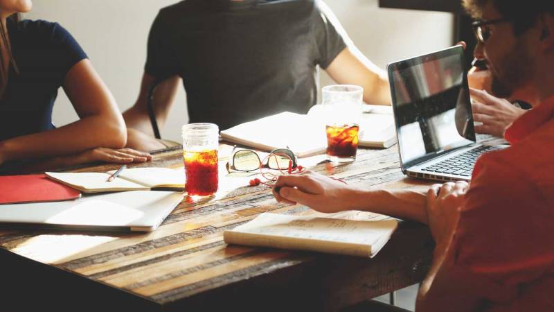 Group of people sitting around a table with notebooks and laptop.