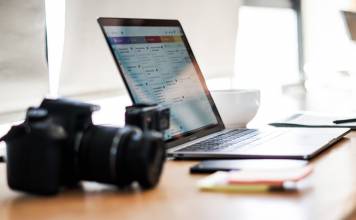camera in the foreground with a computer behind it