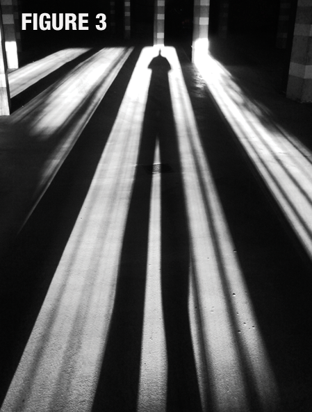 Black and white photo of the long shadow cast by a person across a floor labeled, figure 3. 