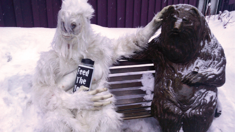 Person in Yeti costume sitting on bench with carved bear.