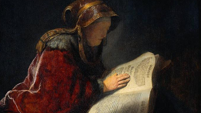 An old woman reads a manuscript with the light from her key streaming in from over her shoulder. 